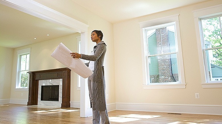Person holding oversized papers looking up while standing in an empty house