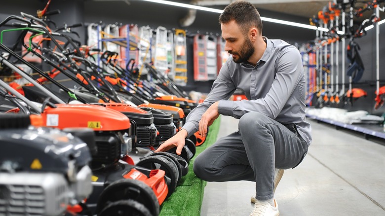 crouched man inspecting line of push mowers in lawn care store