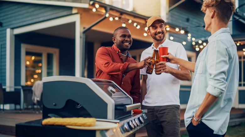 Three smiling men standing around a grill