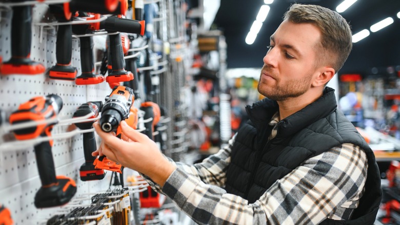 man looking at orange drill in hardware store
