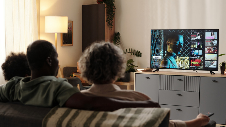 family of three sitting on couch watching television in furnished living room