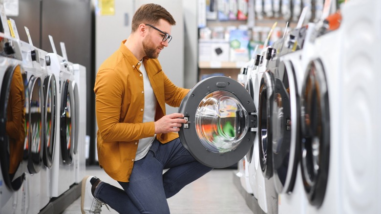 Man kneeling looking inside front load washer in showroom lineup