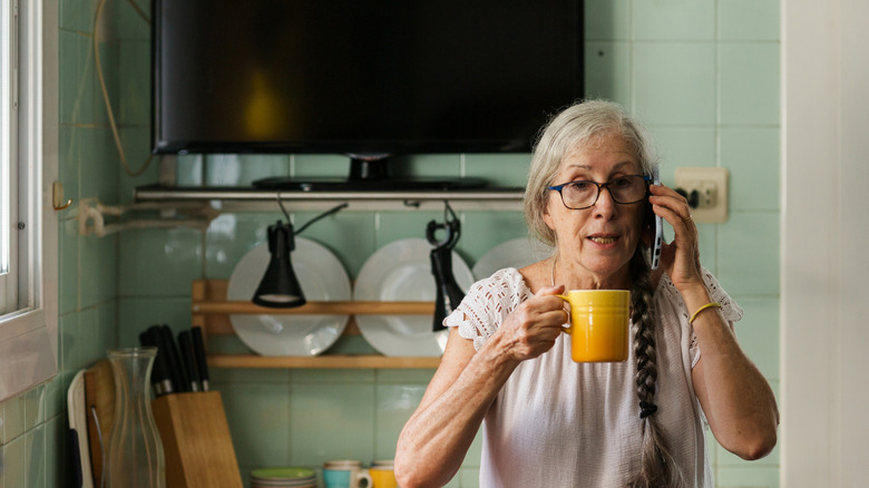 Woman drinking coffee in her kitchen with a TV behind her