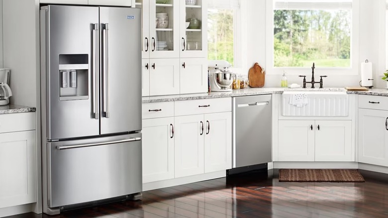 Stainless steel Maytag refrigerator with two drawers and a freezer in a kitchen with white cabinets and wood floors