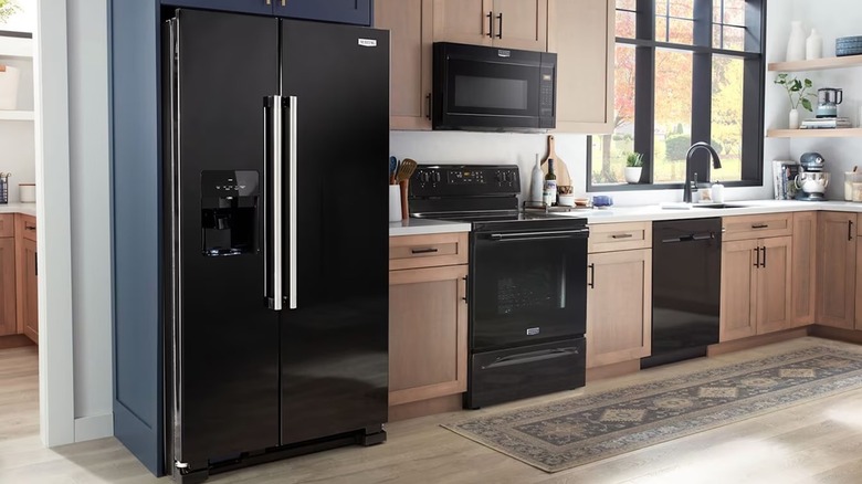Black Maytag refrigerator with side-by-side doors in a kitchen with wooden floors and cabinets