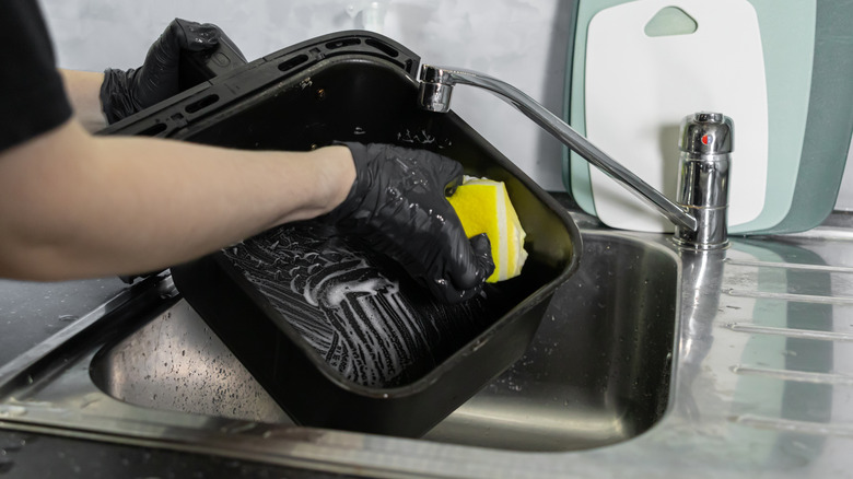 Person washing air fryer basket with soapy sponge.