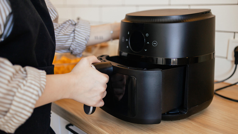 Person opening basket tray of air fryer.