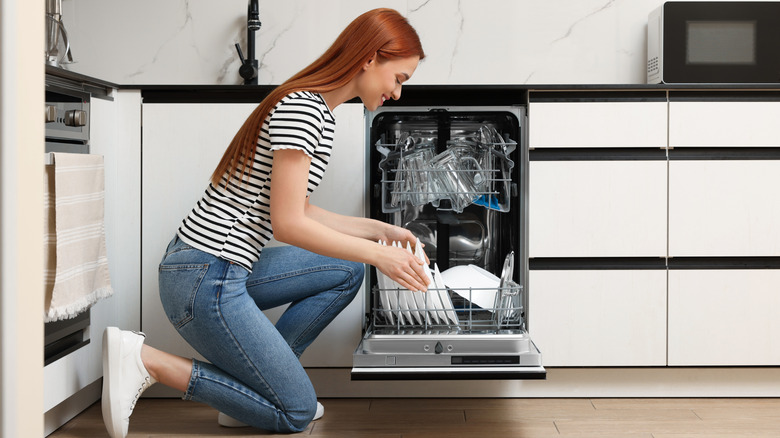 Smiling woman loading dishwasher with plates in kitchen