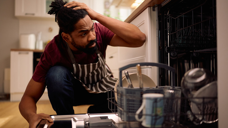 African American man feeling upset about the dishwasher malfunctioning in the kitchen.