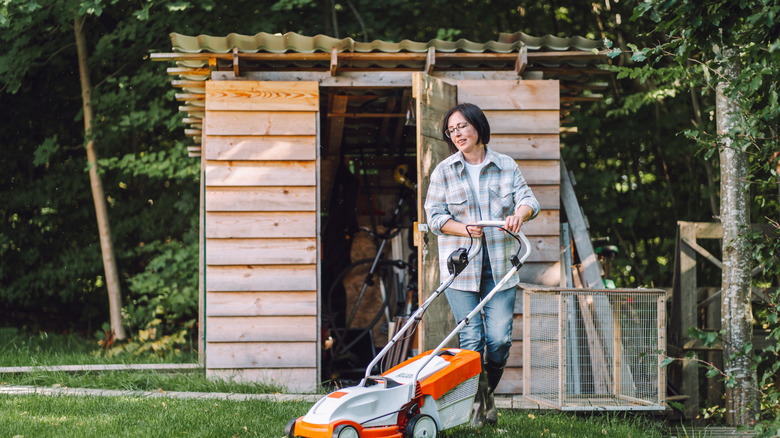Woman pushing a lawn mower near a shed