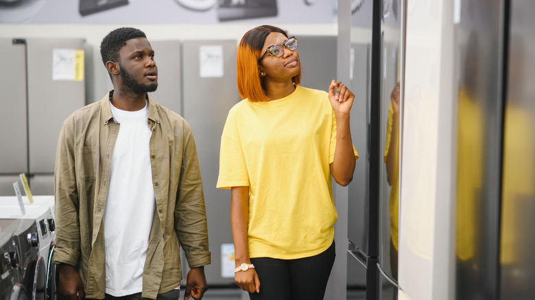 A young Black couple shops for refrigerators at a store.