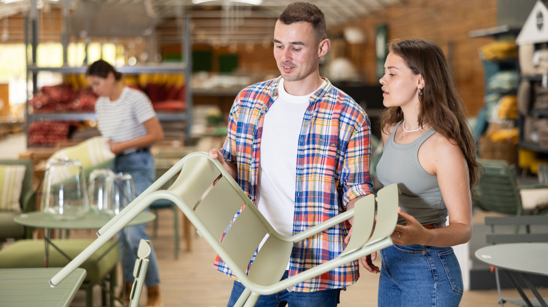 Man and woman holding a green metal chair while shopping for outdoor patio furniture.