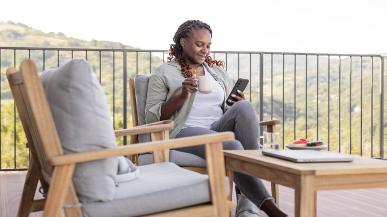Woman looking at smartphone while relaxing on patio furniture.