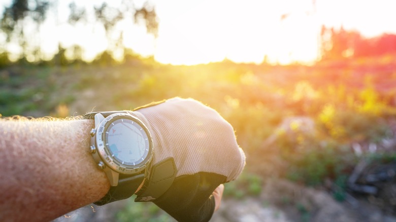 A person checks their watch as the sun sets in the sky