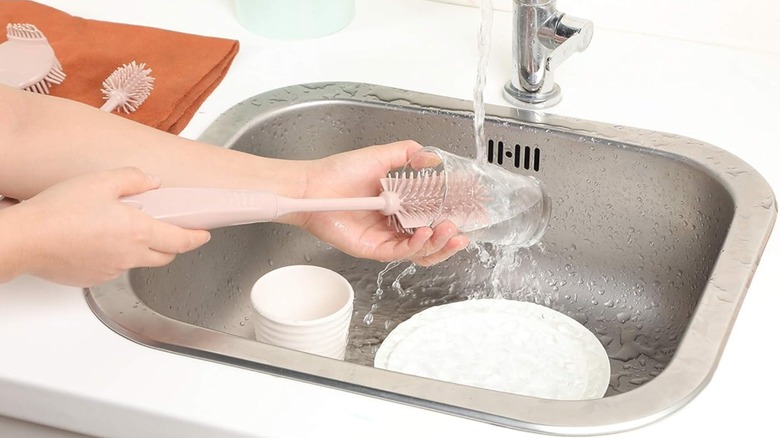 Person's hands using light pink silicone brush to clean clear glass