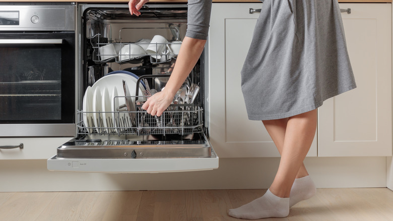 A person's hands are seen loading or unloading a dishwasher in profile.