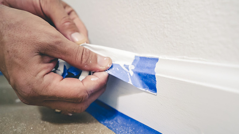 Hand removing blue painter's tape from baseboard