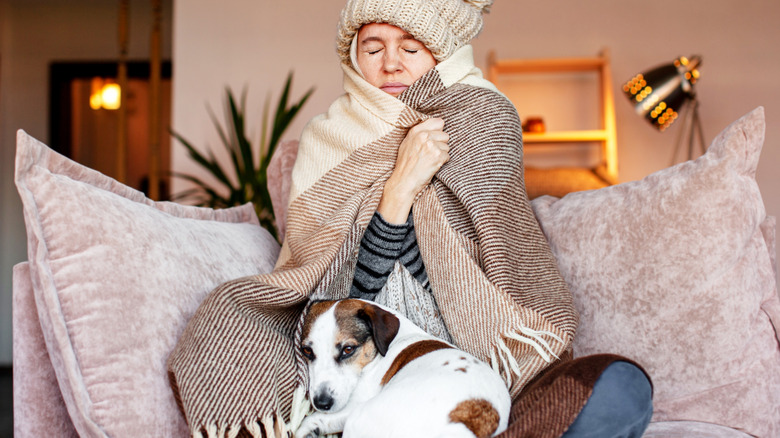 Woman bundled up with blankets and sitting with dog