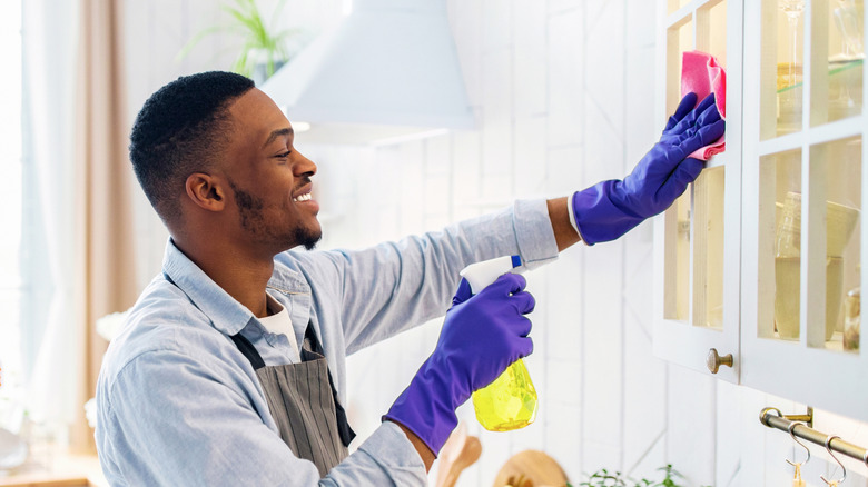 Man cleaning outside of glass-front kitchen cabinets with spray