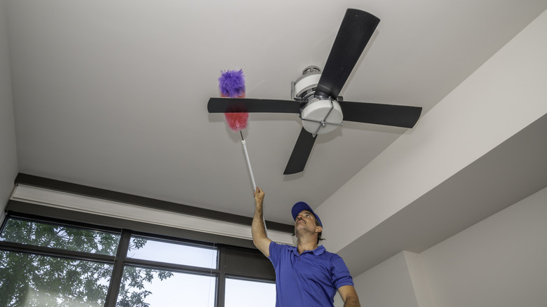 Man using a duster to wipe the blades of a ceiling fan