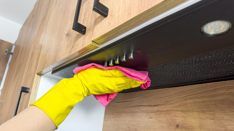 Gloved hand wiping a range hood with a cloth