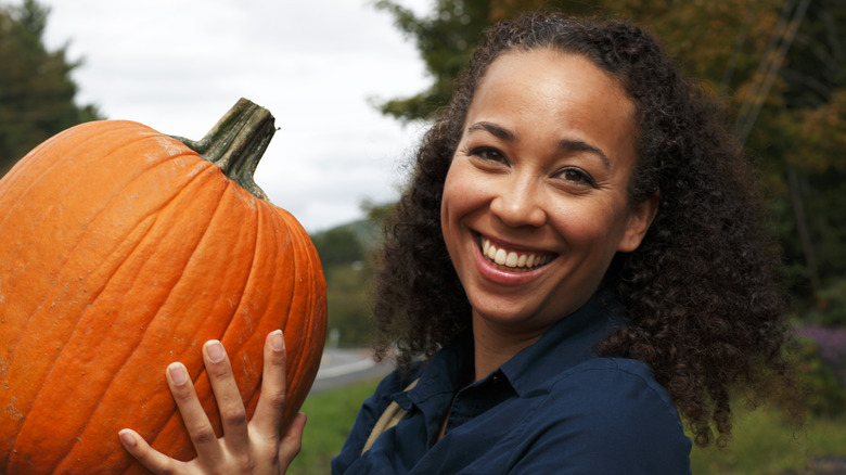 Smiling person holding large pumpkin outside