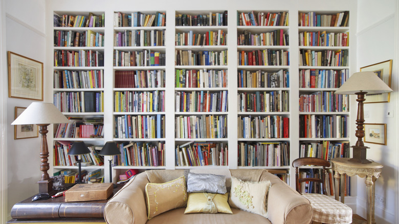 A large built-in bookshelf behind a couch that is overcrowded with books.