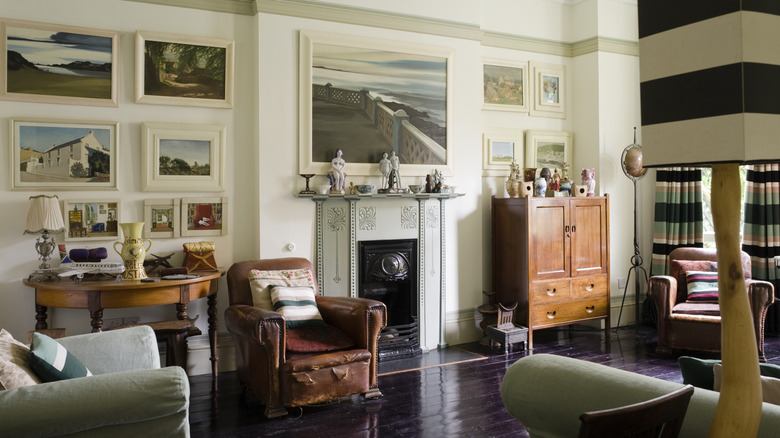 Old money, classic living room area with gallery wall artworks, rich wooden flooring, antique and vintage seating, and ornate fireplace.