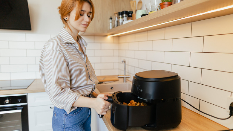 A woman cooking with an air fryer with an oven behind