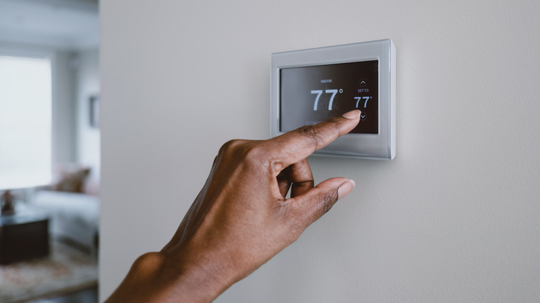 A close up of a hand adjusting the temperature on a thermostat.