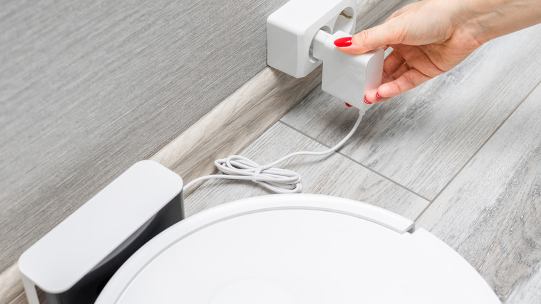 A woman's hand connects a robot vacuum cleaner charger to the power supply