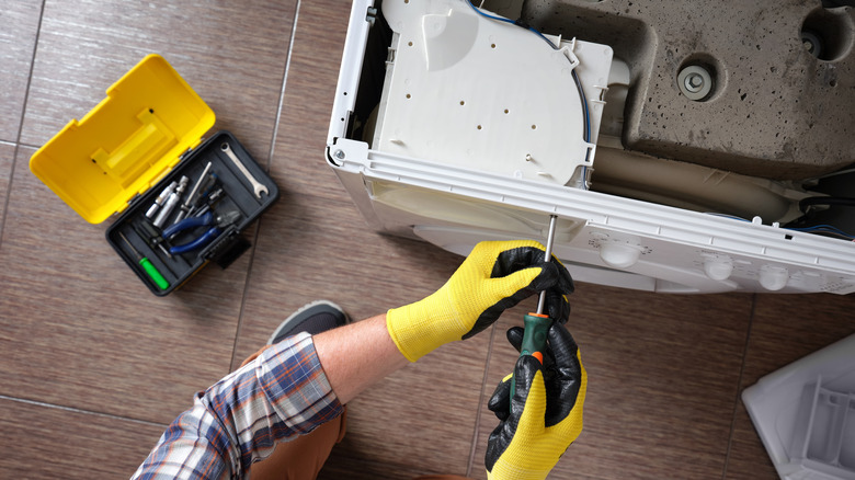 A repairman with screwdriver fixing an appliance.