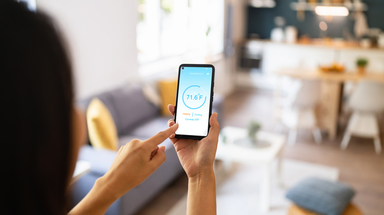 Woman holding phone with running smart home application for temperature control.