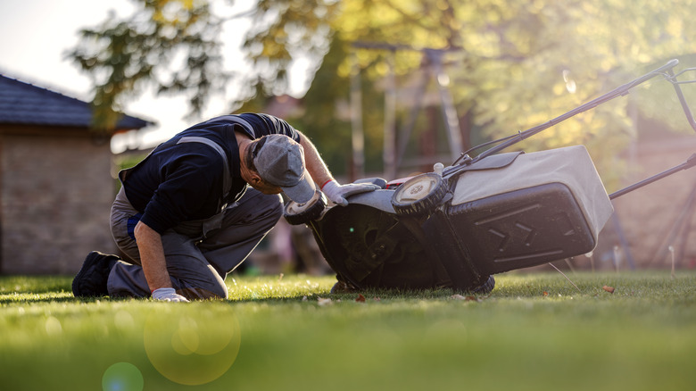 Man kneeling down to look under a lawn mower.