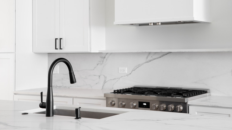 An all white kitchen with white marble countertop and backsplash