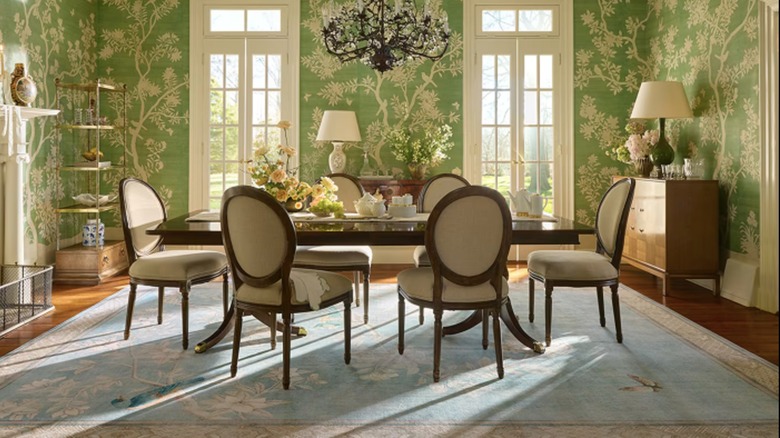 A formal dining room features green chinoiserie wallpaper and light blue chinoiserie-style rug.