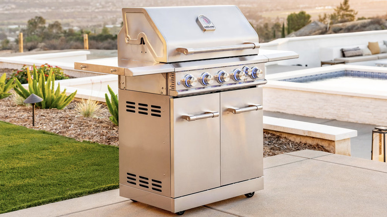 A Kirkland Signature six burner grill made of stainless steel, on a patio next to a pool