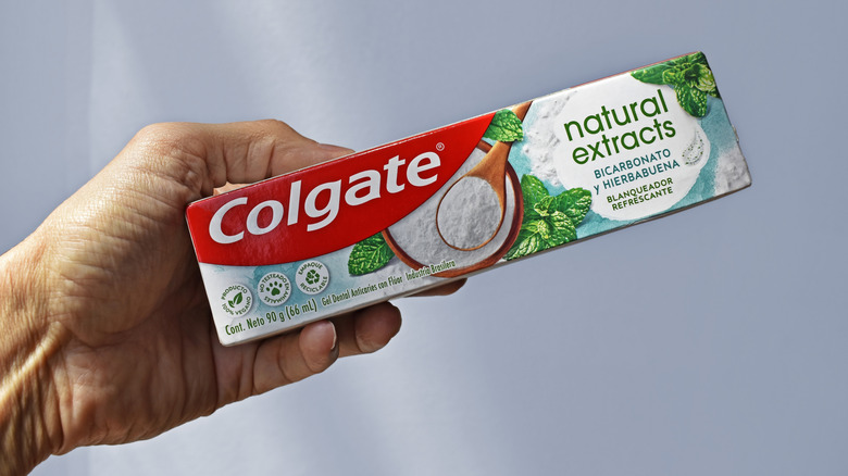 A person holding a box of Colgate natural extracts toothpaste
