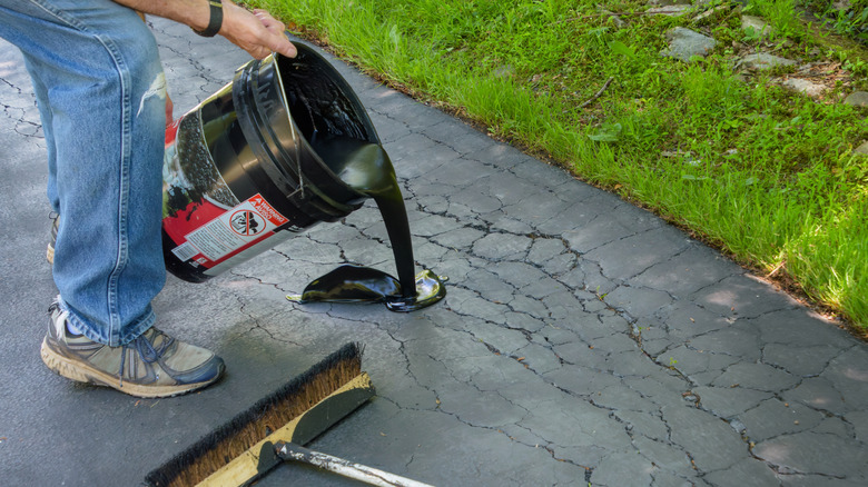 A person pours asphalt on a driveway to repair cracks