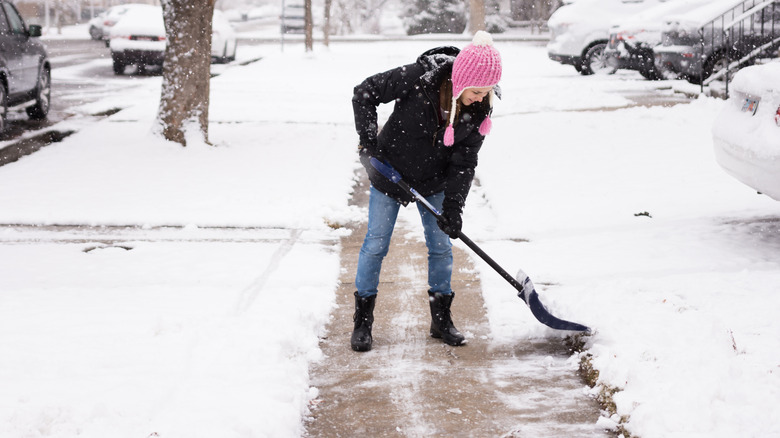 A woman shoveling snow from her sidewalk.
