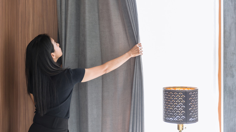 Woman closing curtain while looking up at rod