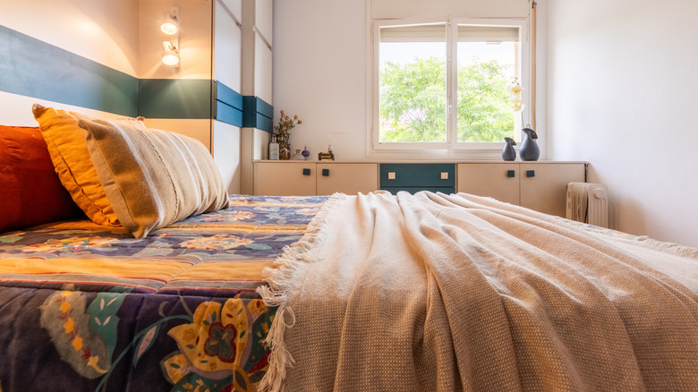 A bed with a patterned quilt in a multicolored patterns and a thin blanket on top