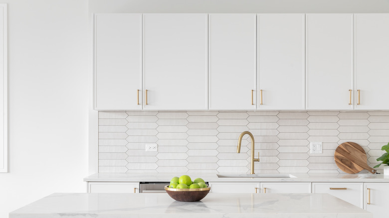 A white kitchen with a basket of green apples on the counter