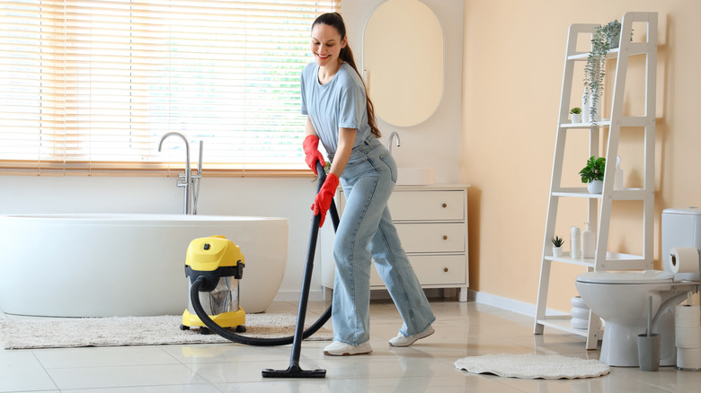Smiling woman wearing red cleaning gloves, vacuuming the bathroom