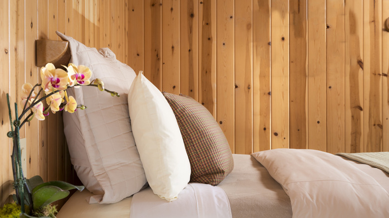 Wood paneled bedroom with bed with sheets, duvet and pillow in neutral colors