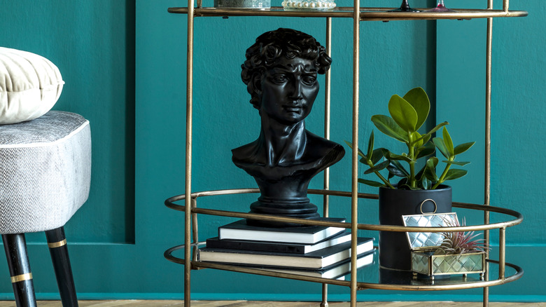 Teal wood paneled wall with metallic rolling cart and black bust