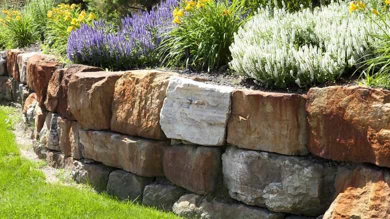 Natural stone retaining wall stacked three rows high with flowers growing above it