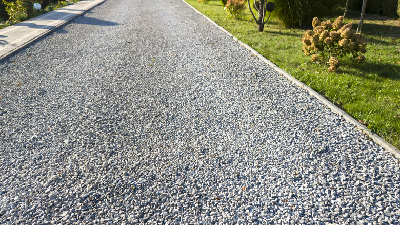 Long gravel driveway lined with grass and flowers