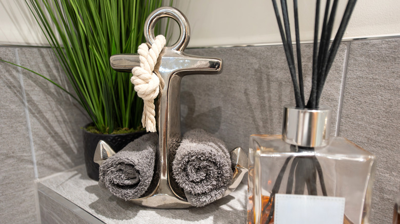 An anchor towel holder sitting on top of a shelf with a plant and essential oil diffuser