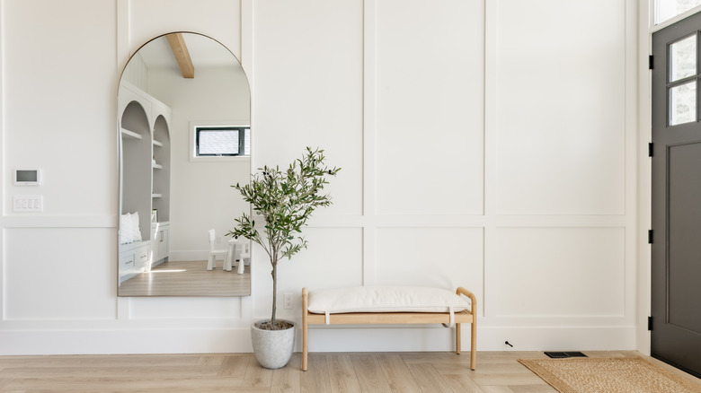 arched mirror in minimal white entryway with black front door